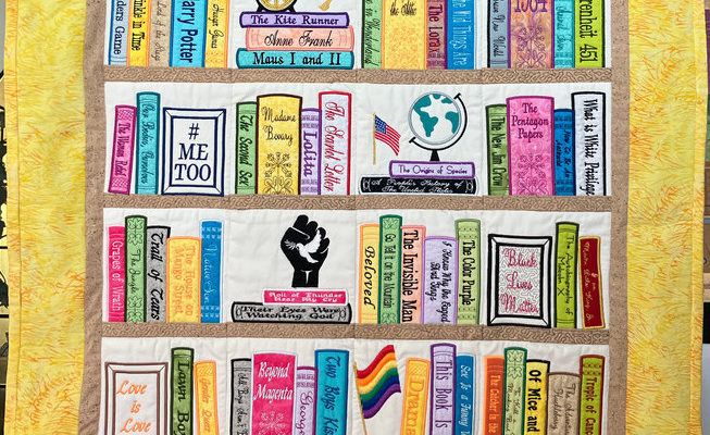 A quilt depicting four bookshelves with books and ideas that have been banned or attacked in the last 100 years. It has a thick yellow order, and the words "Targeted & Banned" embroidered at the top.